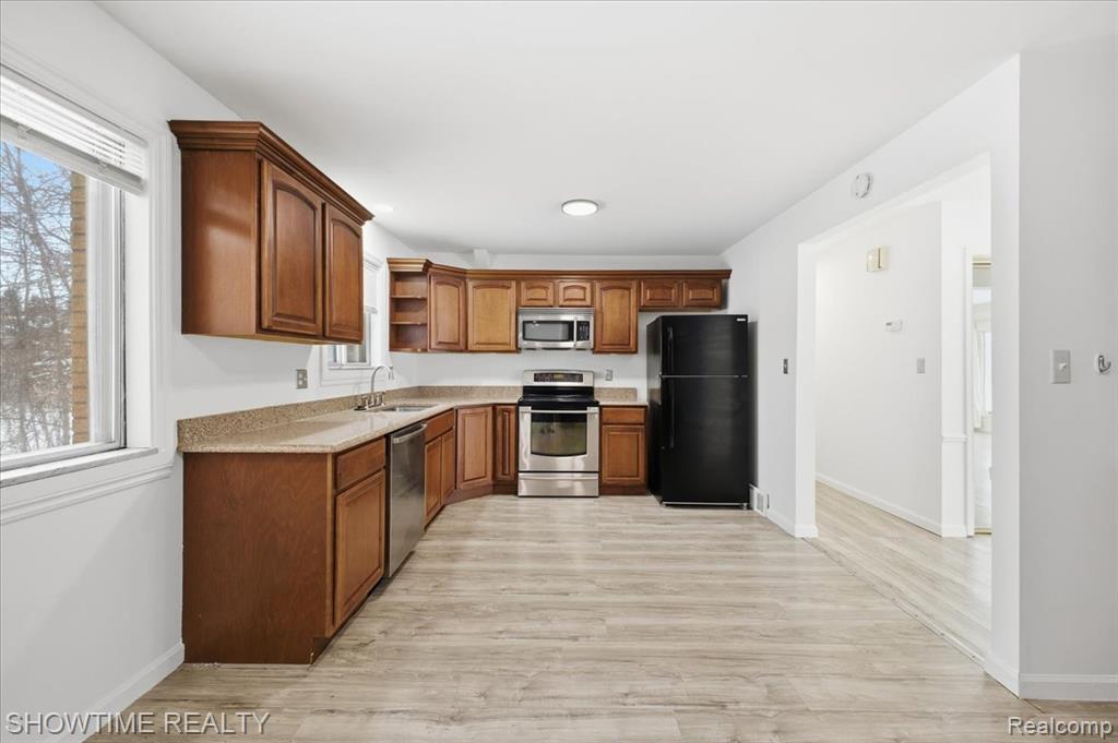 Kitchen featuring open shelves, stainless steel appliances, light wood-type flooring, brown cabinetry, and light stone countertops