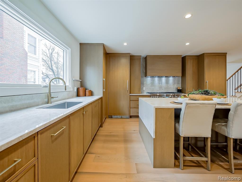 Kitchen featuring a kitchen bar, light stone counters, wall chimney range hood, brown cabinets, and recessed lighting