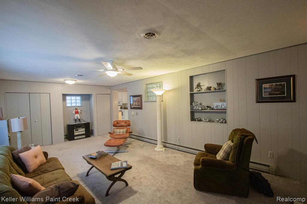 Living area with built in shelves, a textured ceiling, a baseboard radiator, carpet flooring, and a ceiling fan