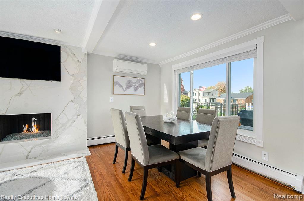 Dining room with a baseboard heating unit, beam ceiling, light wood finished floors, crown molding, and a premium fireplace