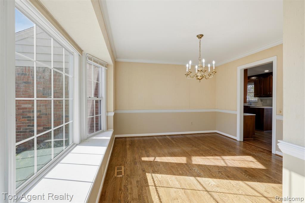 Unfurnished dining area with a chandelier, wood finished floors, and ornamental molding