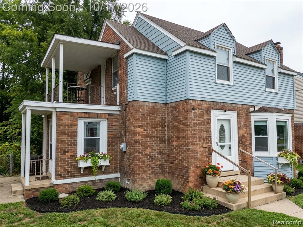 Exterior featuring a combination of brick and vinyl siding, an upper-level covered balcony with metal railing, a covered front entryway, and bay windows
