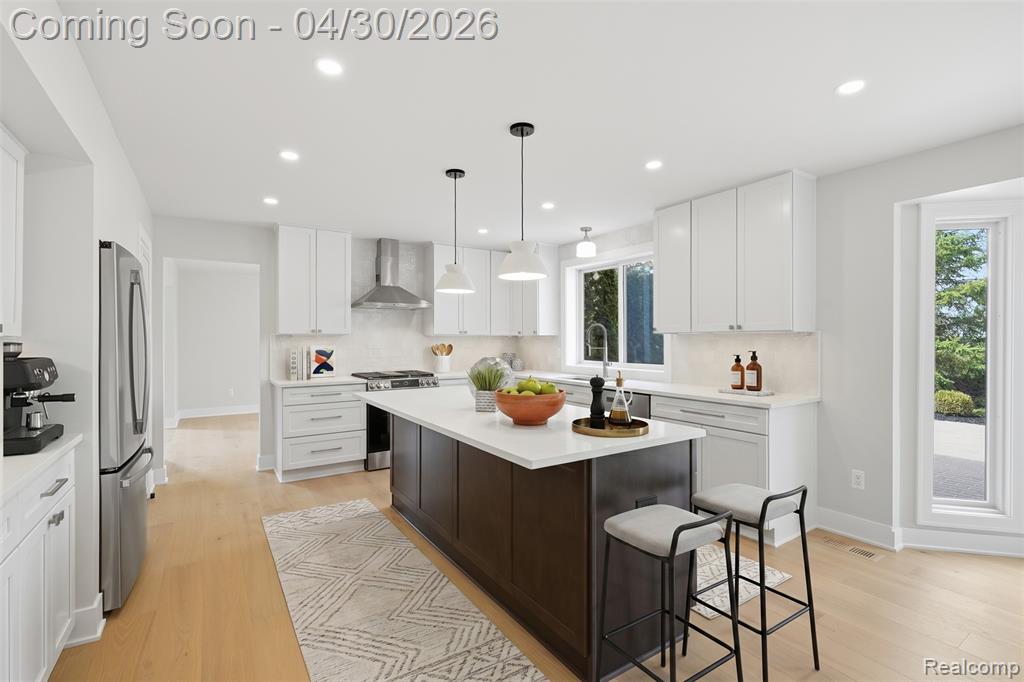 Two tone kitchen featuring a kitchen breakfast bar, a center island, light wood-style flooring, stainless steel appliances, and two tone color scheme