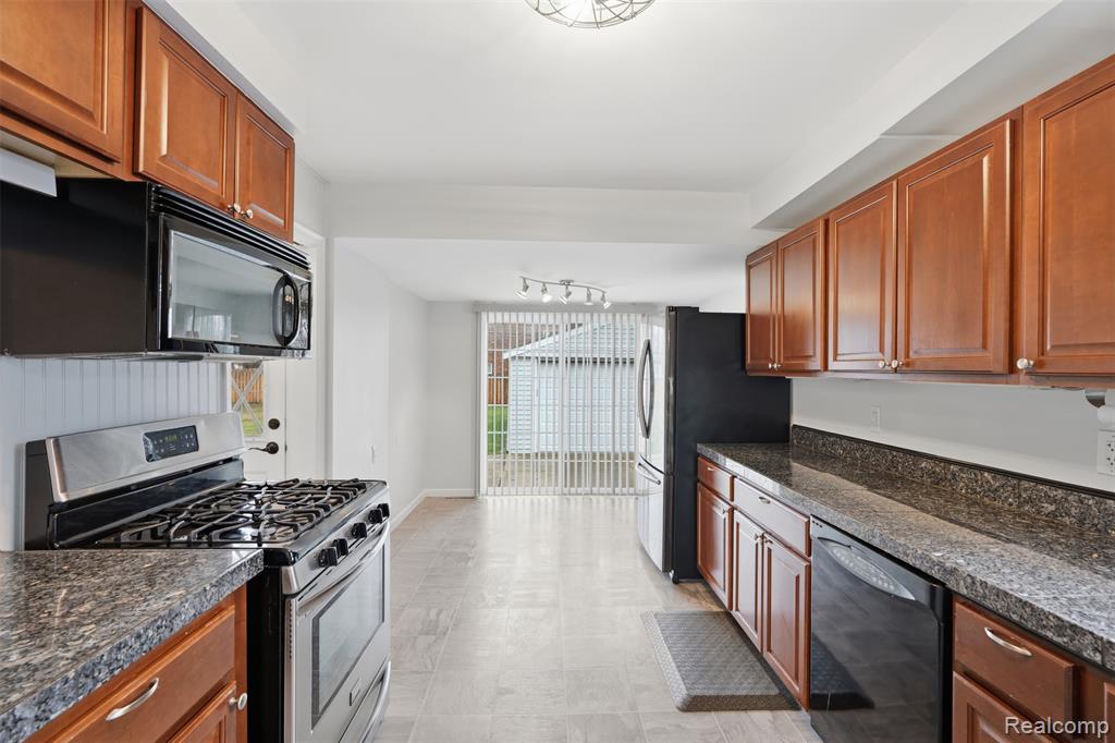 Kitchen with stainless steel appliances, wood finish cabinetry, and dark stone counters