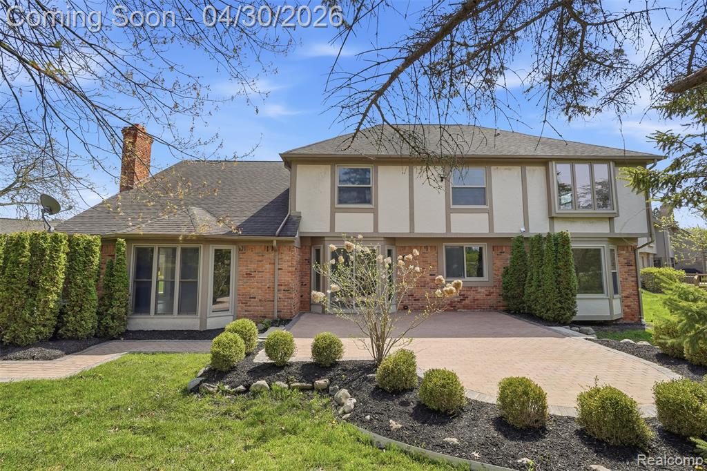 Rear view of property featuring brick siding, stucco siding, a chimney, brick paver patio and mature landscape