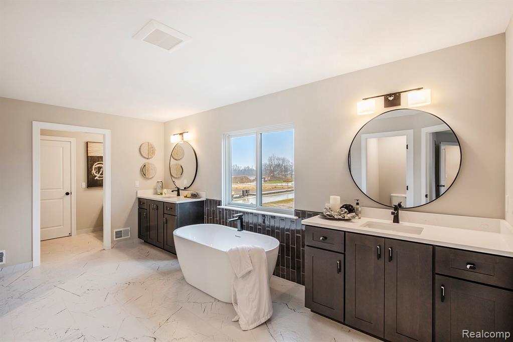 Bathroom with a freestanding bath, two vanities, and light marble finish flooring