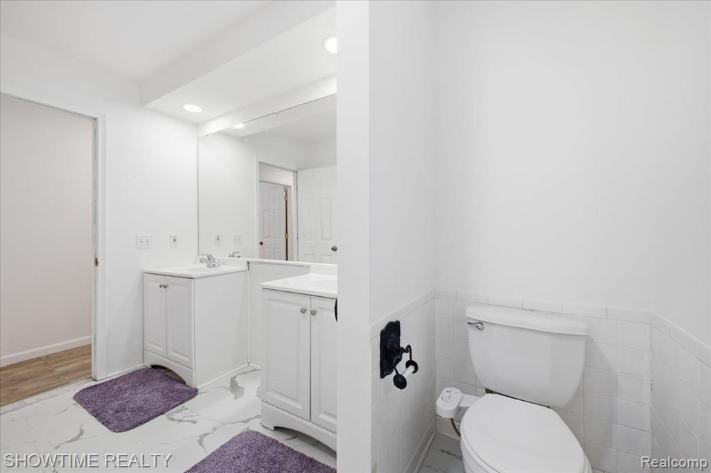 Bathroom featuring light marble finish flooring, two vanities, and recessed lighting