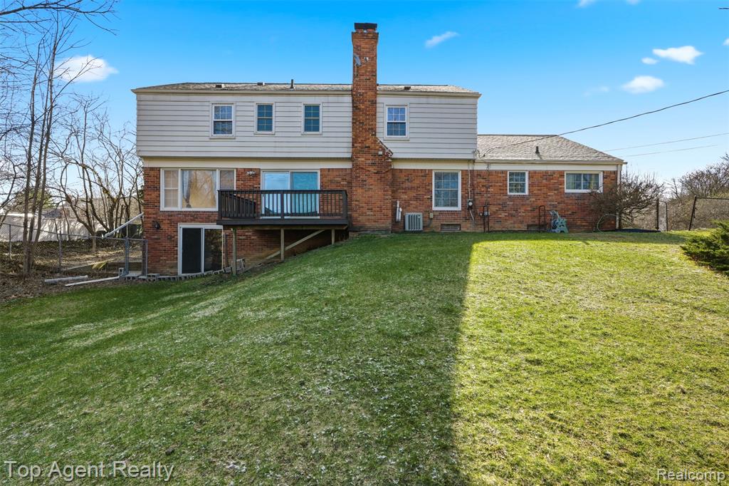 Back of property featuring brick siding, a lawn, a wooden deck, and a chimney