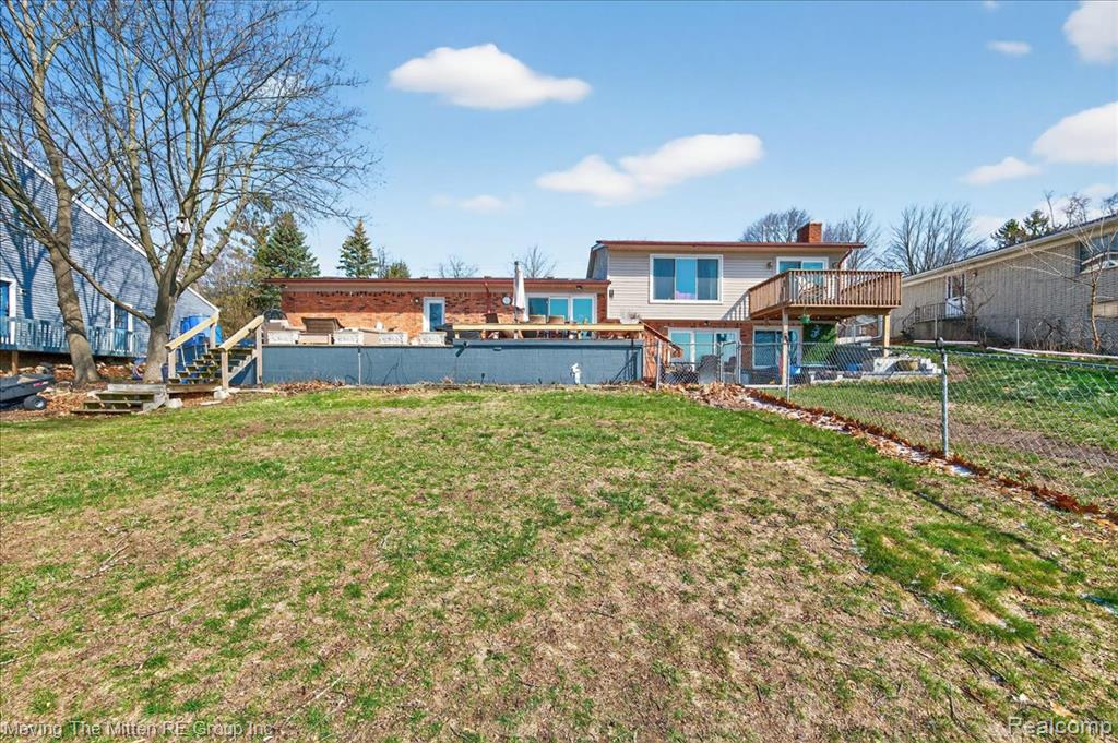 Back of house featuring a wooden deck, a chimney, a pool, and a fenced backyard