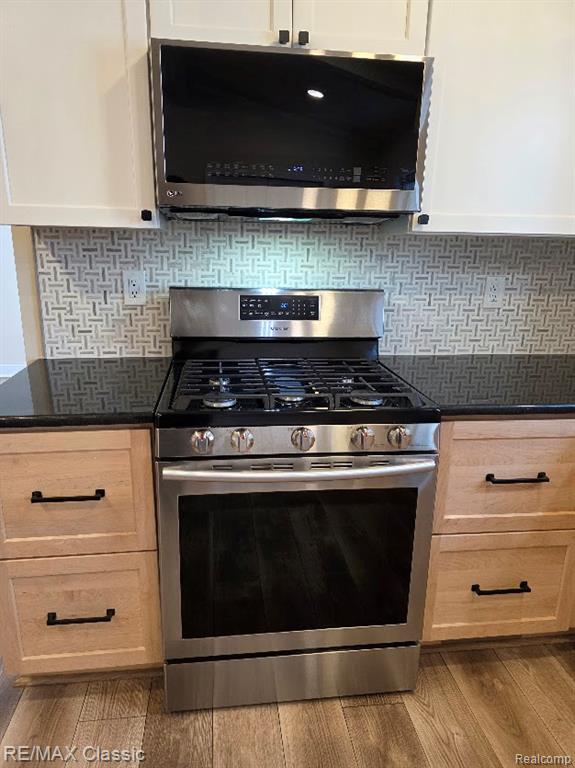 Kitchen featuring stainless steel appliances, decorative backsplash, dark stone counters, and dark wood-style flooring