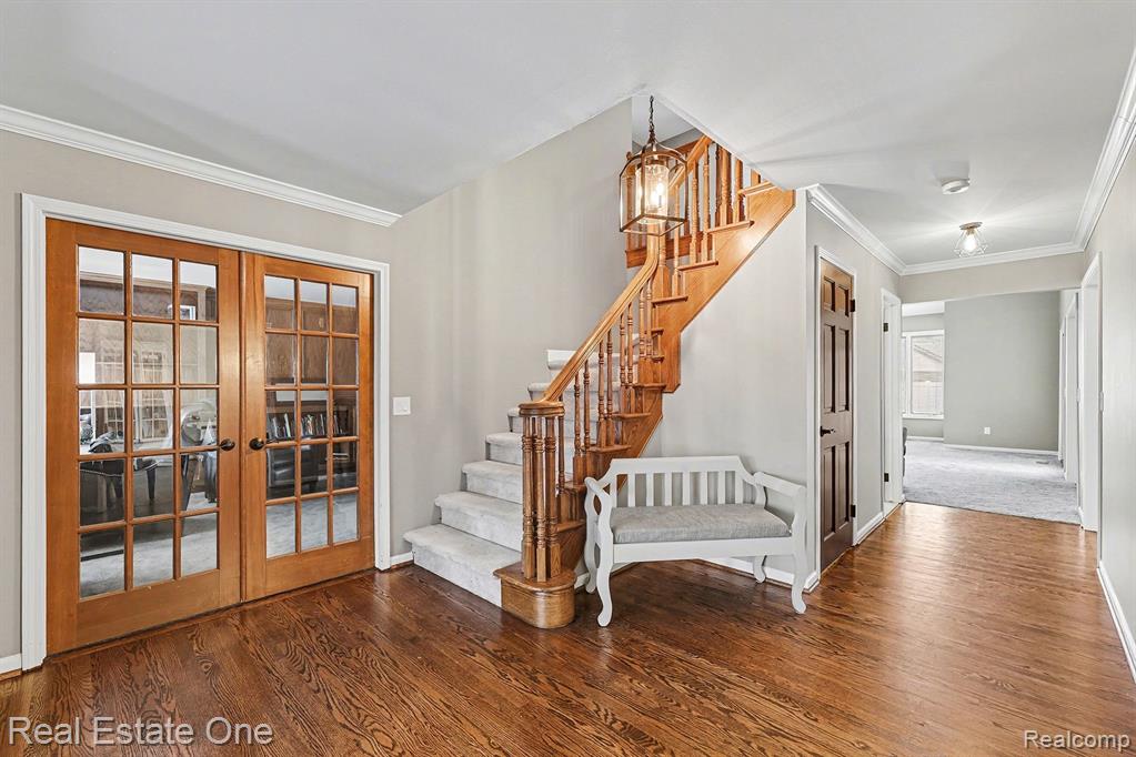 Stairs with crown molding, wood finished floors, french doors, and a chandelier