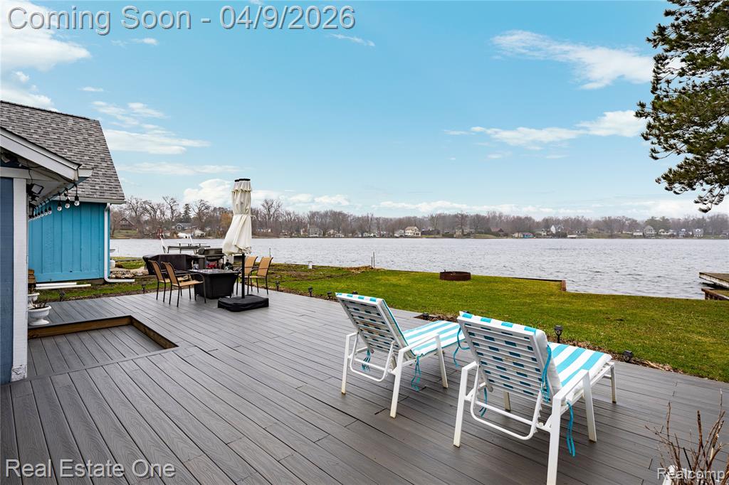 Wooden terrace with a water view, outdoor dining space, and a yard