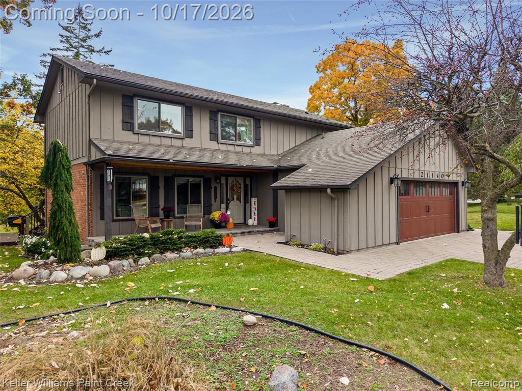 Two-story exterior featuring vertical siding, a covered front porch, brick masonry accents, and a paved driveway leading to an attached garage