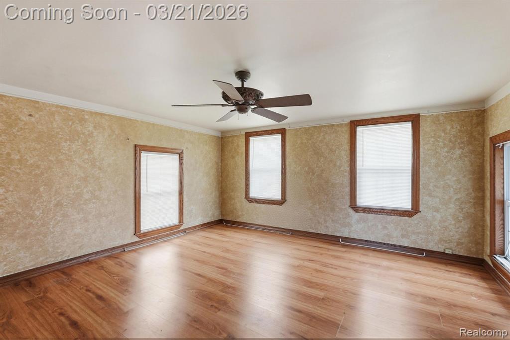 Spare room with a ceiling fan, wallpapered walls, light wood-style flooring, and ornamental molding