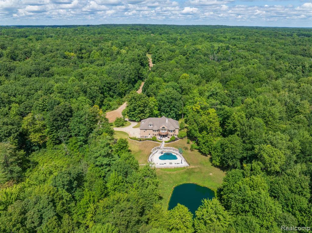 Stone facade residence with a circular drive, private swimming pool, and a pond surrounded by extensive wooded acreage