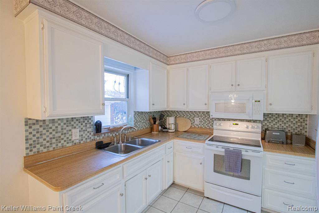 Kitchen with white appliances, light countertops, white cabinetry, light tile patterned floors, and backsplash