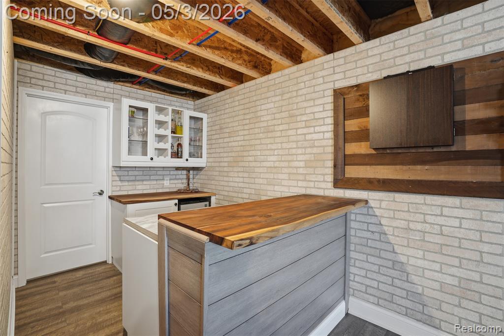 Drybar with wooden counters, brick wall, glass fronted cabinets, white cabinets, and dark wood finished floors
