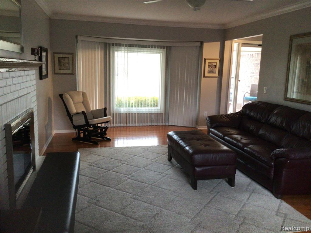 Living room with crown molding, wood finished floors, a fireplace, and ceiling fan