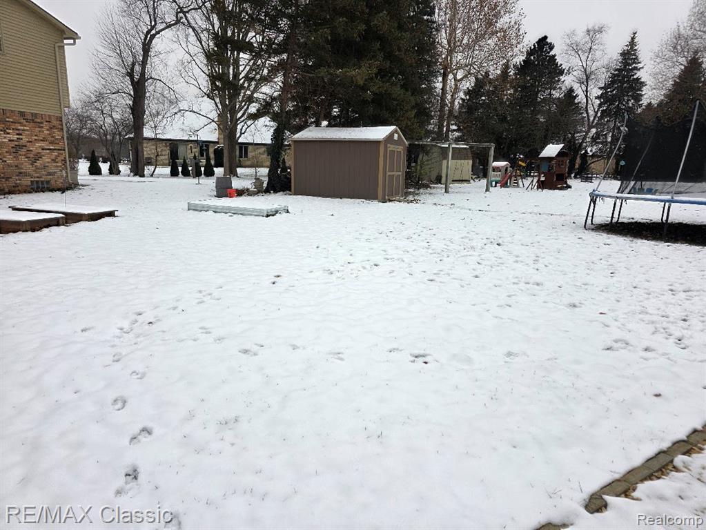 Snowy yard featuring a trampoline and a shed