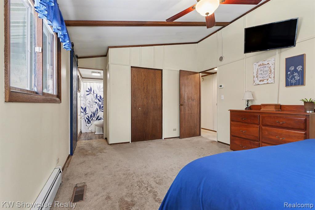 Bedroom with lofted ceiling, a baseboard radiator, ceiling fan, light carpet, and ensuite bath