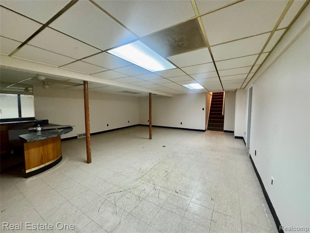 Finished below grade area featuring light flooring, a paneled ceiling, and stairs