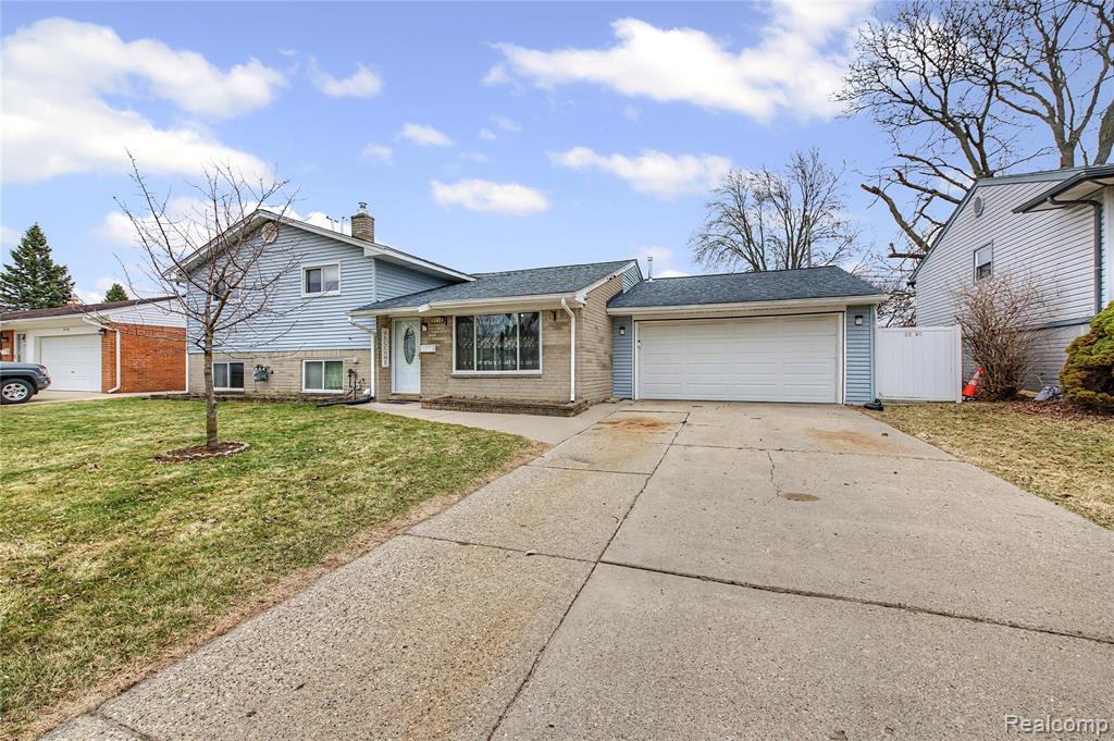 Split level home with a garage, a shingled roof, driveway, and brick siding