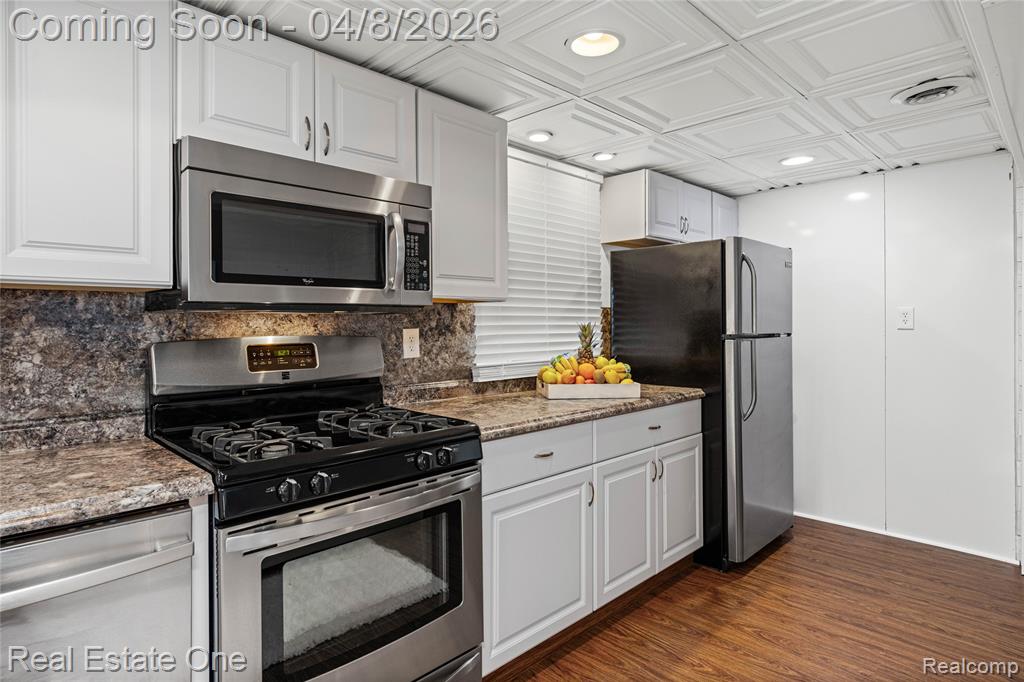 Kitchen with stainless steel appliances, dark wood finished floors, white cabinetry, recessed lighting, and dark stone counters