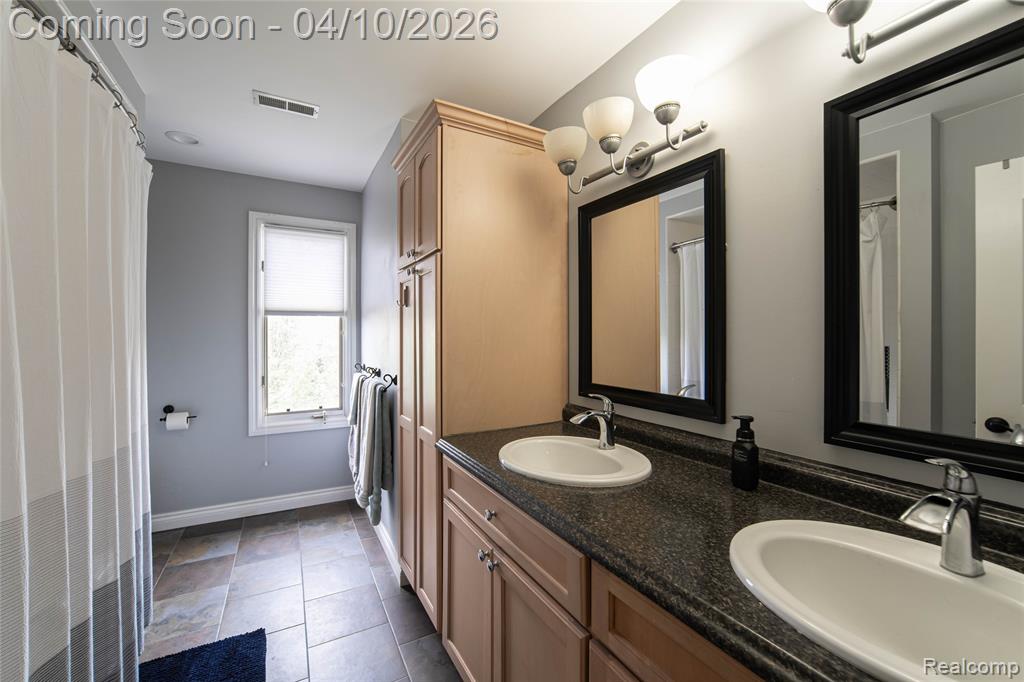 Bathroom with double vanity, dark tile patterned floors, and a shower with curtain