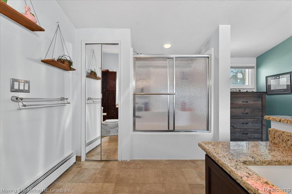 Full bathroom featuring bath / shower combo with glass door, a baseboard radiator, and vanity