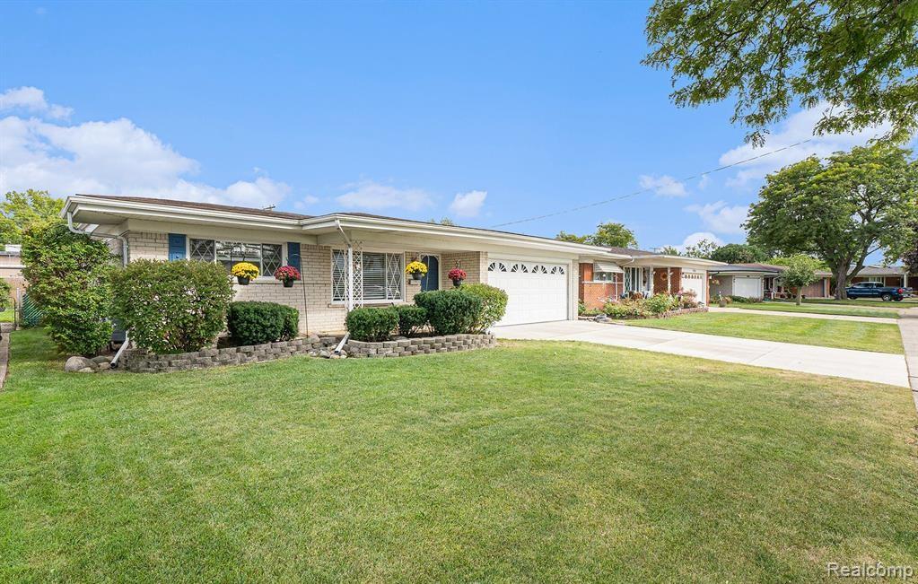Ranch-style home with a front lawn, concrete driveway, brick siding, and a garage