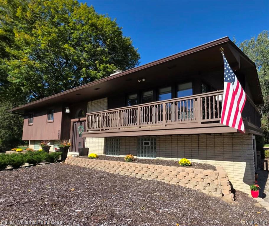 Multi-level exterior featuring a covered wood-railing deck, stacked stone retaining wall, glass block windows, and a combination of wood and masonry siding