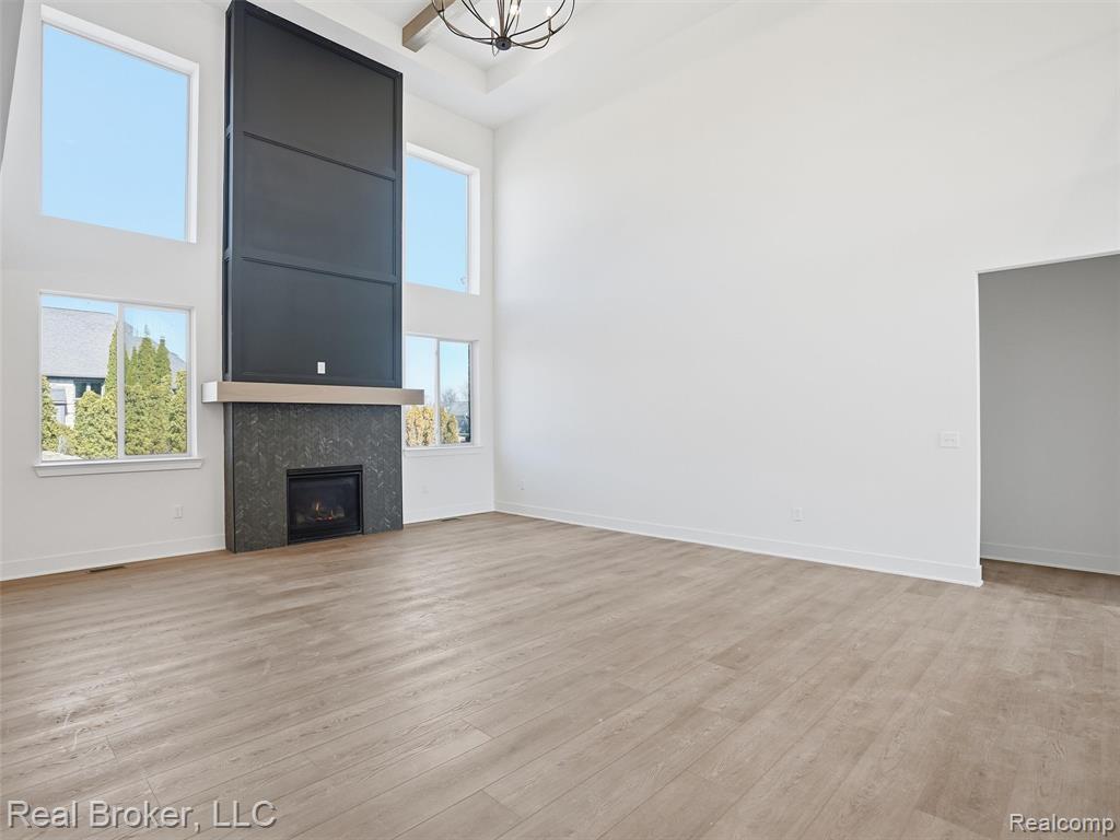 Unfurnished living room with a high ceiling, a fireplace, light wood-style floors, and hanging lights