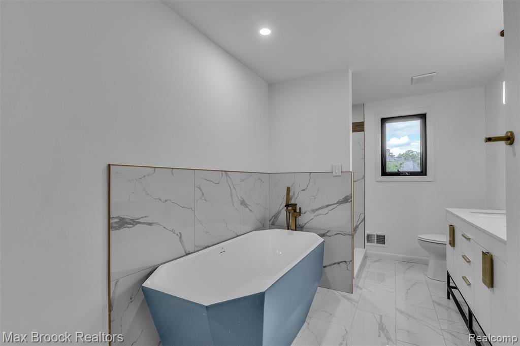 Full bath featuring vanity, a freestanding tub, light marble finish floors, recessed lighting, and tile walls