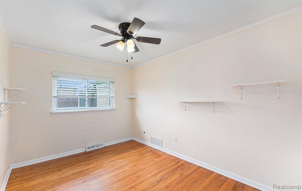 Spare room with crown molding, light wood-style floors, and ceiling fan