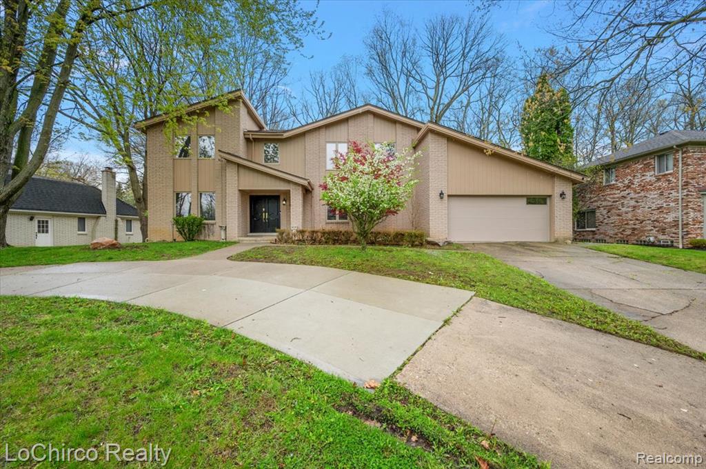 Mid-century home with concrete driveway, brick siding, an attached garage, and a front yard