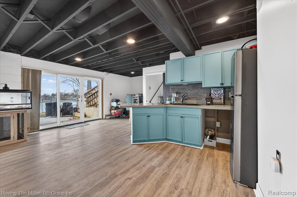 Kitchen with light countertops, freestanding refrigerator, light wood-style flooring, blue cabinetry, and a peninsula
