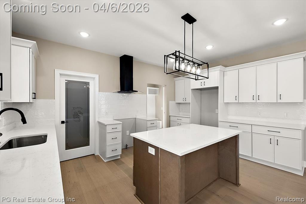 Kitchen featuring light stone countertops, light wood-style floors, decorative backsplash, a kitchen island, and dual tone cabinetry