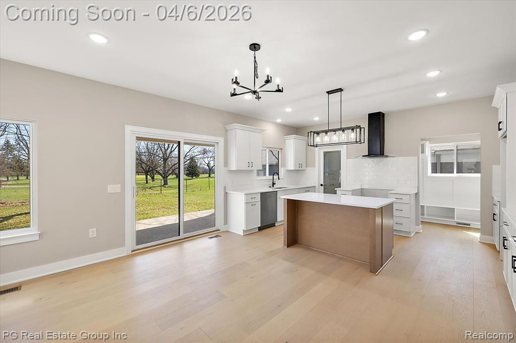 Dual tone kitchen with a center island, two tone color scheme, backsplash, hanging lights, and light wood-style flooring
