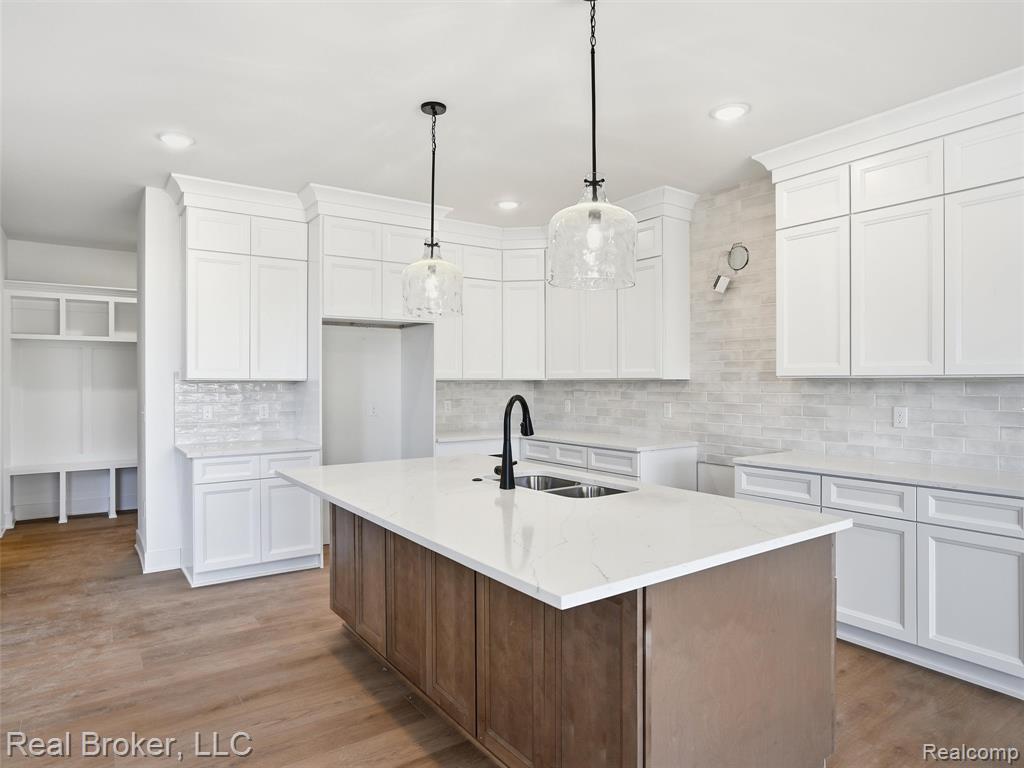 Kitchen featuring a center island with sink, two tone color scheme, light stone countertops, wood finished floors, and decorative backsplash