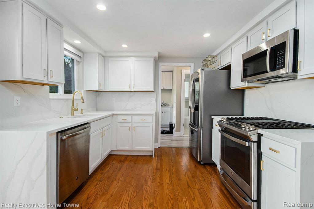 Kitchen with stainless steel appliances, white cabinetry, light stone counters, tasteful backsplash, and dark wood-style floors