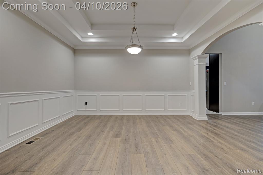 Unfurnished room featuring arched walkways, wainscoting, a decorative wall, light wood-type flooring, and decorative columns