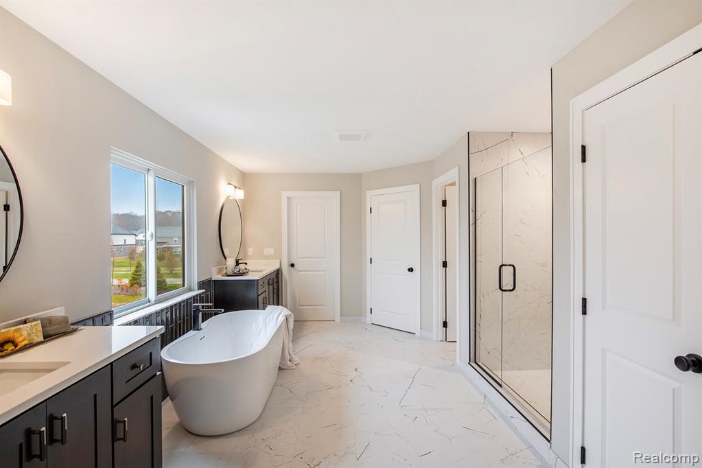 Full bath featuring a freestanding bath, light marble finish flooring, two vanities, and a marble finish shower