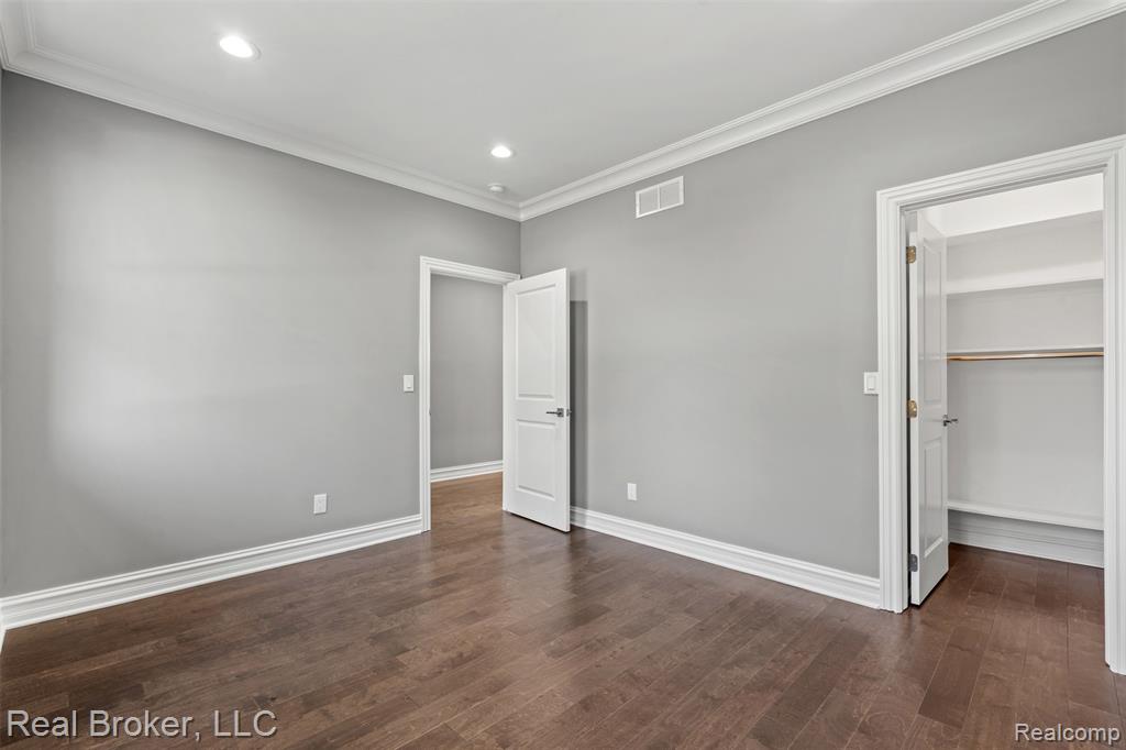 Unfurnished bedroom featuring crown molding, a spacious closet, dark wood-style flooring, and recessed lighting