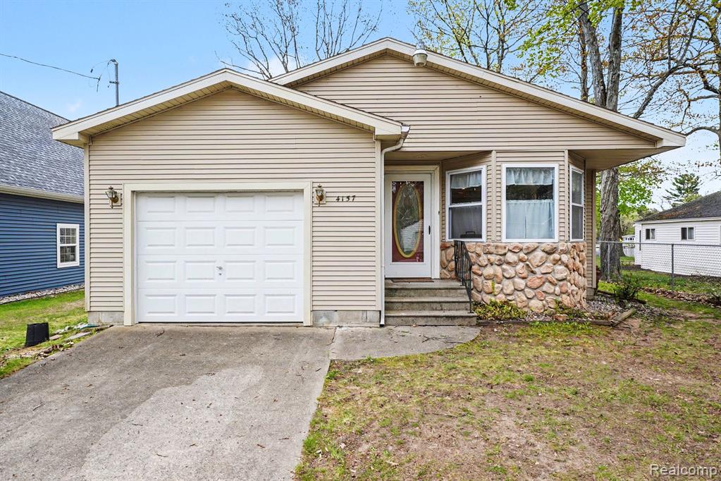 View of front of house with concrete driveway, an attached garage, entry steps, and stone siding