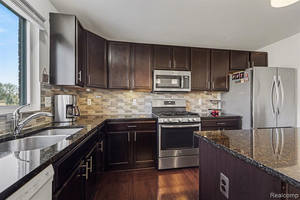 Kitchen featuring stainless steel appliances, dark stone countertops, dark wood finish cabinets, and dark wood-style flooring