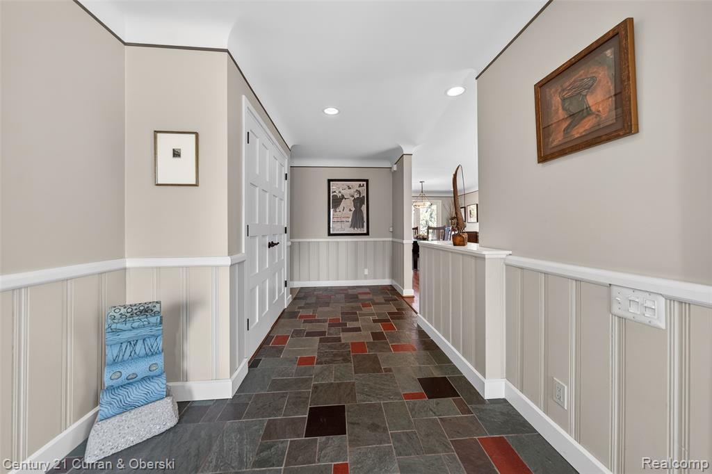 Hall featuring a wainscoted wall, a decorative wall, stone tile flooring, and recessed lighting