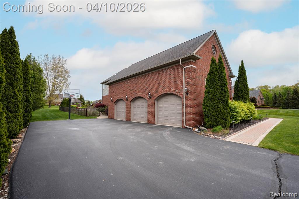 View of side of property with brick siding, a garage, asphalt driveway, and a shingled roof