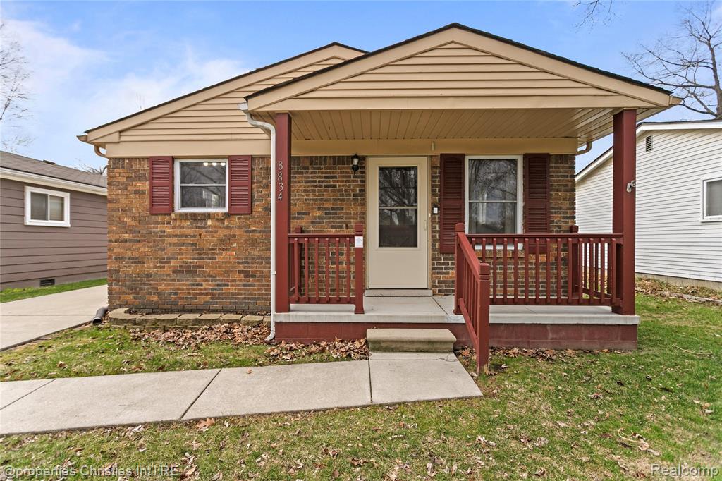 Bungalow featuring covered porch, brick siding, and a front yard