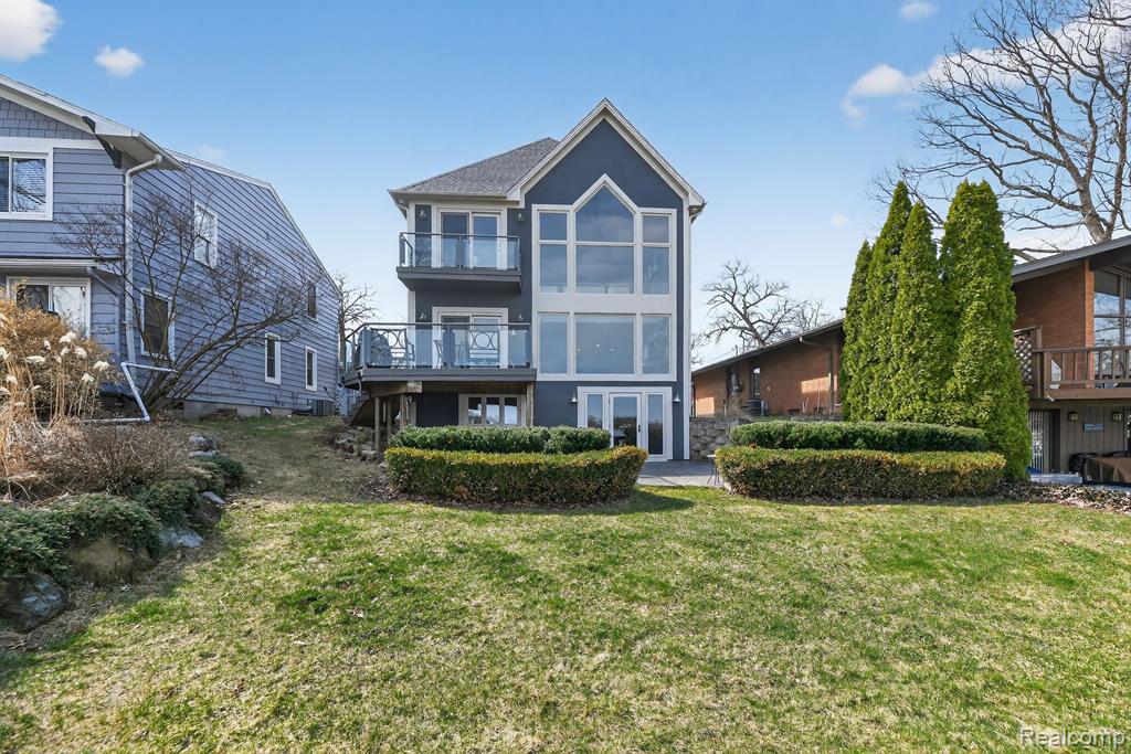 Back of property featuring a lawn, a balcony, and stucco siding
