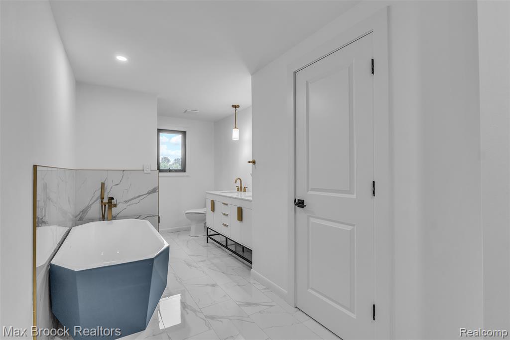 Full bath with a freestanding bath, vanity, light marble finish floors, and recessed lighting